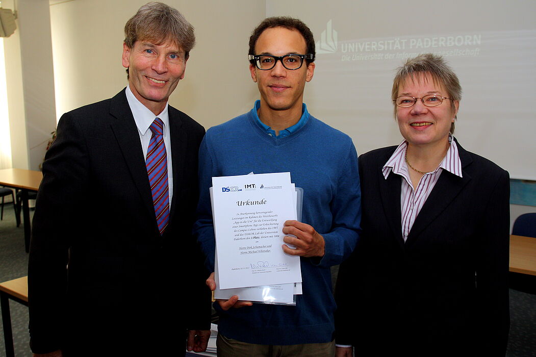Foto (Universität Paderborn, Patrick Kleibold): Prof. Dr. Nikolaus Risch und Prof. Dr. Leena Suhl überreichen die Urkunde für den ersten Preis im Wettbewerb „App in die Uni“ an Michael Whittaker für dessen App „I-UPB“.