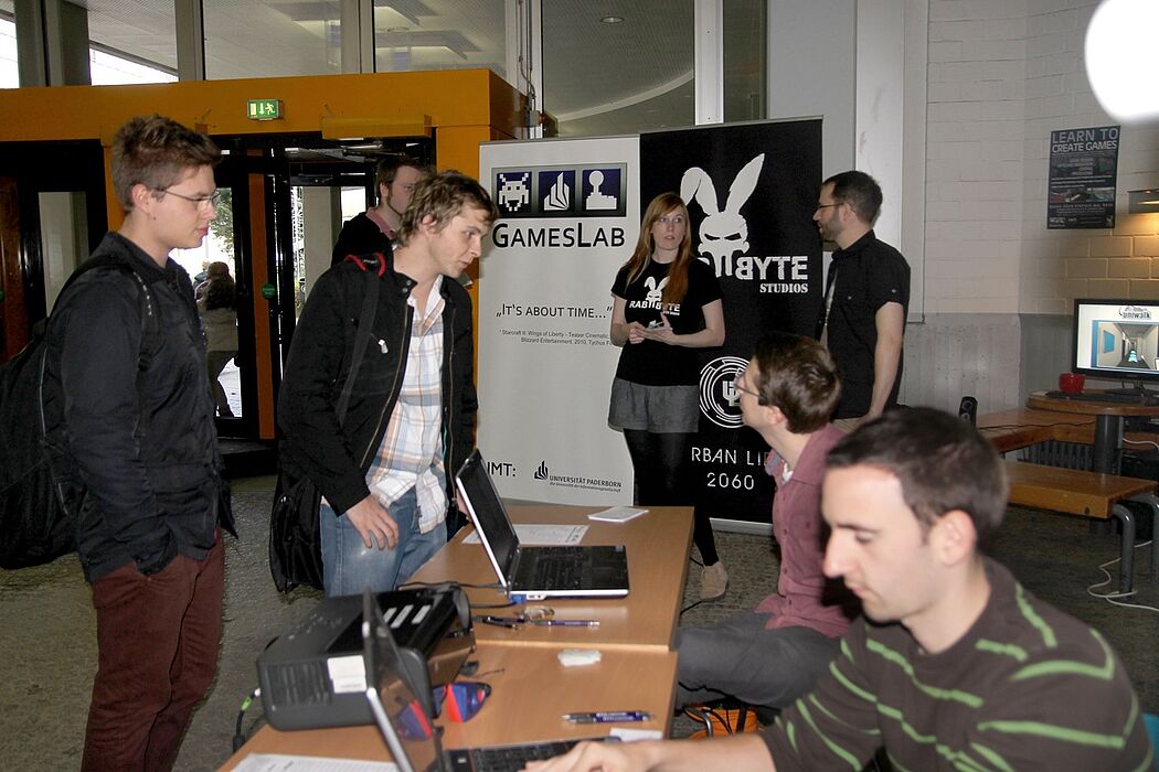 Foto (Lena Schäfer): Markus Mertens (vorne rechts am Tisch sitzend), Paul Hemsen (vorne links am Tisch sitzend), Lukas Kemper (im Hintergrund, halb verdeckt) sowie Franzi Schlots und Volker Spaarmann (beide vom Gameslab) mit Studenten.